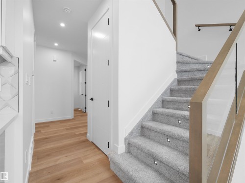 Staircase featuring light gray carpeting, integrated step lighting, and a wood-finish handrail with glass panels - 214 Crystal Creek Drive, Leduc, AB 
