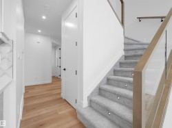 Staircase featuring light gray carpeting, integrated step lighting, and a wood-finish handrail with glass panels - 