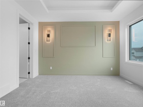 Carpeted interior space featuring a tray ceiling, an accent wall with decorative trim, two wall-mounted light fixtures, and a large window - 214 Crystal Creek Drive, Leduc, AB 