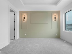 Carpeted interior space featuring a tray ceiling, an accent wall with decorative trim, two wall-mounted light fixtures, and a large window - 