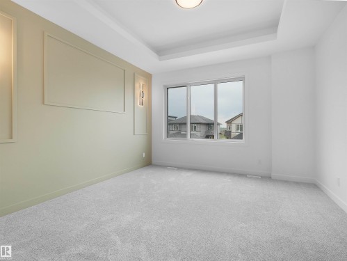 Spacious room featuring tray ceilings, neutral carpeting, and a large window - 214 Crystal Creek Drive, Leduc, AB 