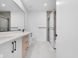 Contemporary bathroom featuring a double vanity with stone countertops, integrated sinks, and matte black hardware - 