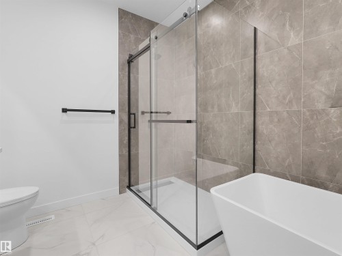 Spacious bathroom featuring a glass-enclosed shower with matte black framing, a freestanding soaking tub, and large format wall tiles with a natural stone appearance - 214 Crystal Creek Drive, Leduc, AB 