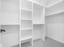 Custom closet system featuring white built-in shelving, multiple hanging rods, and light gray carpet flooring - 