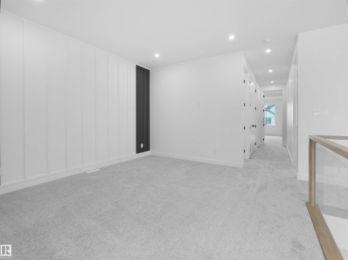Spacious carpeted room featuring a white panel accent wall with a dark vertical accent, recessed lighting, and a contemporary glass and wood-finish railing - 214 Crystal Creek Drive, Leduc, AB 