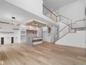 Expansive open-concept interior featuring light wood-finish flooring, a contemporary kitchen island with a dark faucet, white cabinetry with wood accents, and a multi-level staircase with glass railings - 214 Crystal Creek Drive, Leduc, AB 