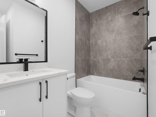 Bathroom featuring a white vanity with a white countertop and integrated sink, a large framed mirror, and a bathtub with tiled surround - 214 Crystal Creek Drive, Leduc, AB 