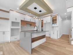 Open-concept kitchen featuring an island with a waterfall countertop, light wood-finish flooring, white and wood-tone cabinetry, a geometric tile backsplash, and recessed and pendant lighting - 