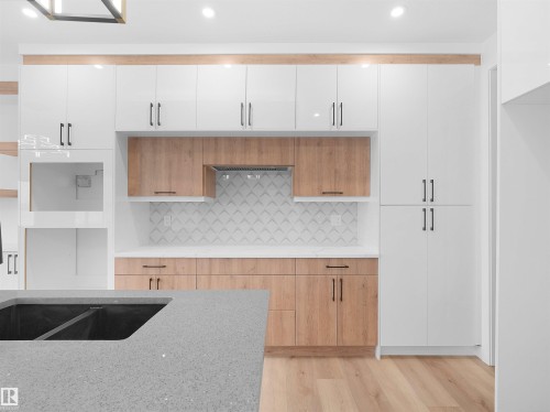 Modern kitchen featuring a light wood-finish flooring and a large island with a dark sink - 214 Crystal Creek Drive, Leduc, AB 