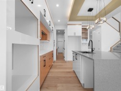Modern kitchen featuring an expansive island with a waterfall-edge countertop and undermount sink, sleek white cabinetry, wood-finish flooring, and contemporary pendant lighting - 