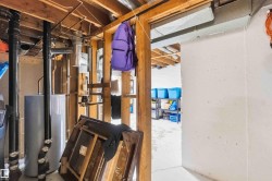 Basement utility area featuring exposed joists, visible plumbing, a water heater, and a concrete floor - 
