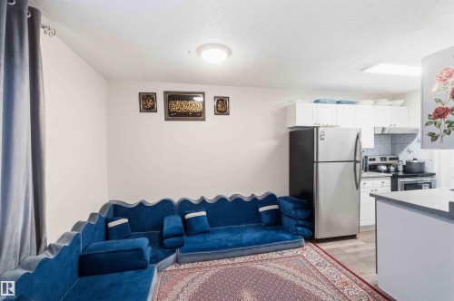 Open-concept living area featuring wood-finish flooring, a contemporary ceiling light fixture, and a kitchen area with white cabinetry and stainless steel appliances - 203 11421 34 Street Nw, Edmonton, AB 