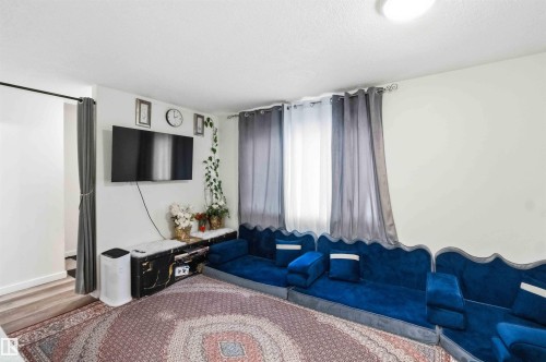 Living area featuring a wall-mounted television, a black marble-look media console, and a bright overhead light fixture - 203 11421 34 Street Nw, Edmonton, AB 