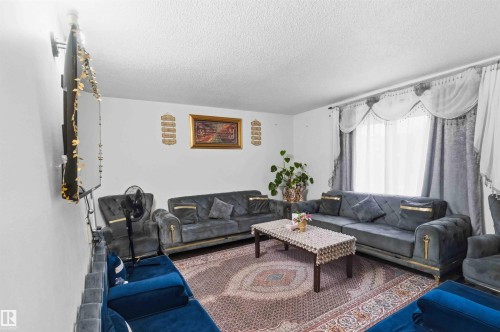 Living area featuring a textured ceiling, a window with decorative drapes, and a wall-mounted television bracket - 203 11421 34 Street Nw, Edmonton, AB 