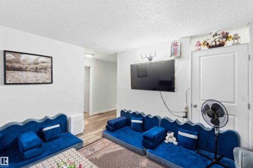 Living area featuring light gray walls, wood-finish flooring, a wall-mounted television, and a white paneled door - 203 11421 34 Street Nw, Edmonton, AB 