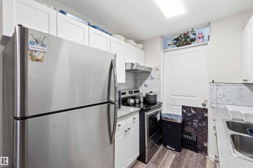 Compact kitchen featuring stainless steel appliances, white cabinetry, laminate countertops, and wood-finish flooring - 203 11421 34 Street Nw, Edmonton, AB 