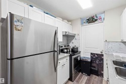 Compact kitchen featuring stainless steel appliances, white cabinetry, laminate countertops, and wood-finish flooring - 