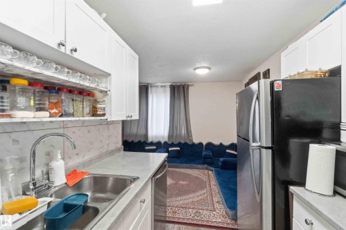 Galley-style kitchen featuring white cabinetry, a stainless steel sink with a high-arc faucet, and light-toned countertops - 203 11421 34 Street Nw, Edmonton, AB 