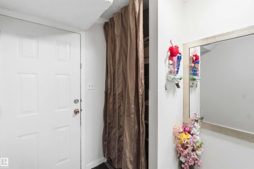 White paneled door with brass-toned hardware, complemented by a textured ceiling and a full-length mirror with a light-toned frame - 203 11421 34 Street Nw, Edmonton, AB 