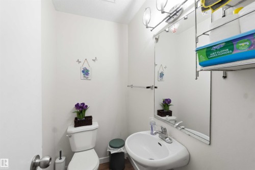Compact bathroom featuring a white wall-mounted sink with a chrome faucet, a wall-mounted mirror, a two-piece toilet, and overhead vanity lighting - 203 11421 34 Street Nw, Edmonton, AB 