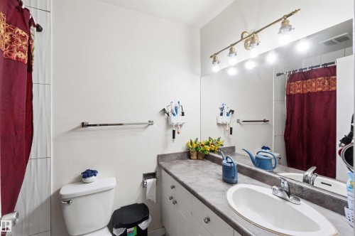 Full-width vanity mirror with a four-light brass fixture, white oval undermount sink, and a gray countertop - 203 11421 34 Street Nw, Edmonton, AB 