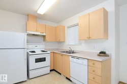 Kitchen featuring light wood cabinetry with brass-toned hardware, white appliances, and a double basin stainless steel sink - 