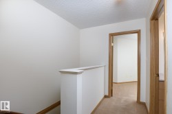 Upper level landing featuring light neutral wall paint, wood-finish door frames, and textured ceiling - 