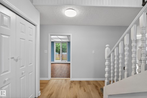 Entryway featuring wood-finish flooring, white paneled bifold doors, a classic white staircase, and an overhead flush-mount light fixture - 14808 55 Street, Edmonton, AB 