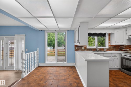 Kitchen area featuring white cabinetry, brick-style backsplash, white tile-finish countertops, and wood-finish flooring - 14808 55 Street, Edmonton, AB 