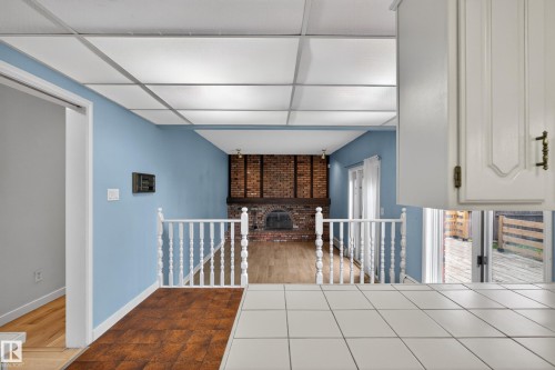 Living space featuring a brick fireplace with a wood mantle, light wood-finish flooring, and white spindle railing - 14808 55 Street, Edmonton, AB 