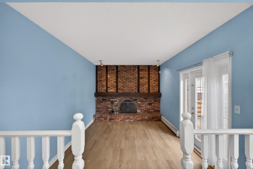 Brick fireplace with dark wood mantel, wood-finish flooring, white double doors with transom windows, white baluster railings, and track lighting - 14808 55 Street, Edmonton, AB 