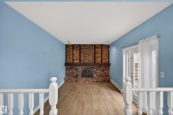 Brick fireplace with dark wood mantel, wood-finish flooring, white double doors with transom windows, white baluster railings, and track lighting - 