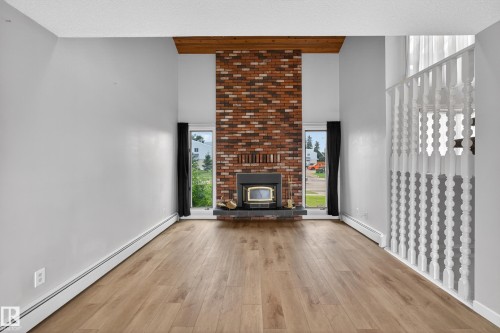 Vaulted ceiling living space featuring a floor-to-ceiling brick fireplace with a dark-toned hearth and wood-burning insert - 14808 55 Street, Edmonton, AB 
