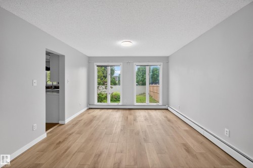 Spacious room featuring wood-finish flooring, light grey painted walls, white baseboards, and a contemporary flush-mount ceiling light - 14808 55 Street, Edmonton, AB 