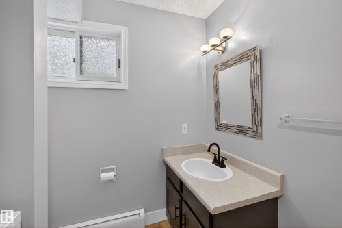 Bathroom featuring a vanity with a light-toned countertop, an undermount sink, and a dark-finish faucet - 14808 55 Street, Edmonton, AB 