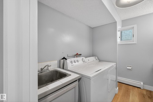 Dedicated laundry area featuring a utility sink with tile surround, wood-finish flooring, and a window for natural light - 14808 55 Street, Edmonton, AB 