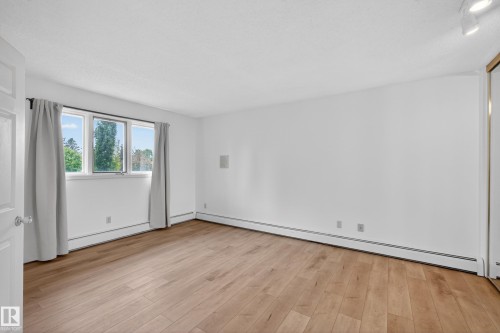 Spacious interior room featuring wood-finish flooring, white walls, and a large window with multiple panes - 14808 55 Street, Edmonton, AB 
