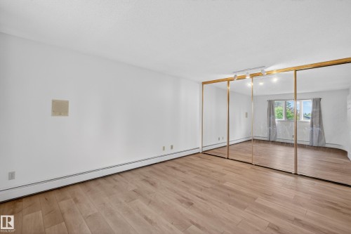 Spacious room featuring wood-finish flooring, white walls, and a full wall of mirrored closet doors with gold-toned trim - 14808 55 Street, Edmonton, AB 