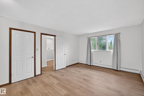 Hardwood-finish flooring throughout, featuring a multi-pane window with exterior scenery, white interior doors with dark wood trim, and baseboard heating - 14808 55 Street, Edmonton, AB 