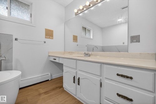 Bathroom featuring a single vanity with light-toned countertop, integrated sink, and wood-finish flooring - 14808 55 Street, Edmonton, AB 