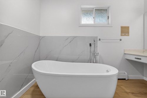 Freestanding soaking tub with chrome fixtures, set against a backdrop of large format marble-look wall tiles - 14808 55 Street, Edmonton, AB 