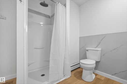 Full bathroom featuring a walk-in shower with built-in shelving, a rainfall showerhead, a commode, and wood-finish flooring - 14808 55 Street, Edmonton, AB 