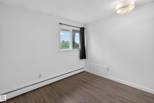 Room featuring wood-finish flooring, white baseboards, a window with exterior views, and a modern ceiling light fixture - 14808 55 Street, Edmonton, AB 