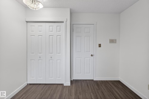 White bi-fold doors with round silver pulls, wood-finish flooring, white baseboards, and a contemporary ceiling light fixture - 14808 55 Street, Edmonton, AB 