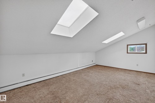 Attic space featuring two skylights, a single window, white painted walls, and brown carpeting - 14808 55 Street, Edmonton, AB 