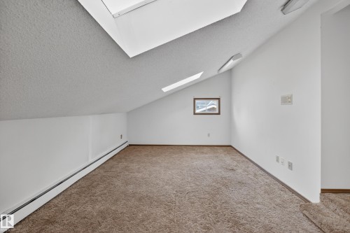 Sloped ceiling room featuring two skylights, brown carpet flooring, and white painted walls - 14808 55 Street, Edmonton, AB 