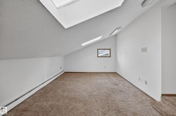 Sloped ceiling room featuring two skylights, brown carpet flooring, and white painted walls - 