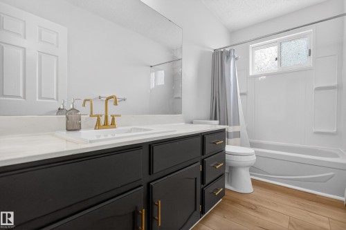 Bathroom vanity featuring a white countertop, undermount sink, and brass-finish faucet - 14808 55 Street, Edmonton, AB 