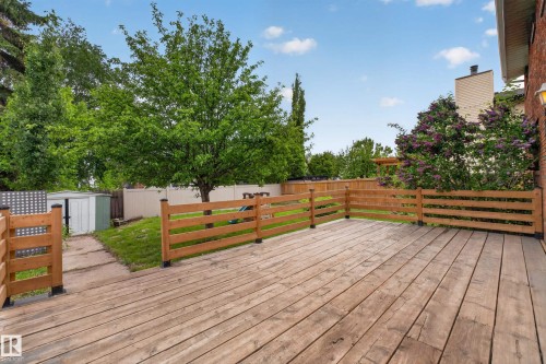 Expansive wooden deck with a slatted wood railing, surrounded by mature trees and greenery - 14808 55 Street, Edmonton, AB 