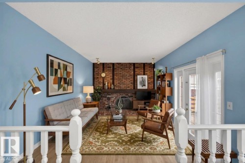 Living area featuring a brick fireplace, wood-finish flooring, vaulted ceiling, and white balustrade - 14808 55 Street, Edmonton, AB 